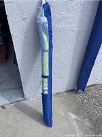 Photo of the beach umbrella in its blue carrying bag standing against a wall, showing overall storage condition.