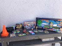 Wide view of all items on wooden bench outdoors, showing a mix of toys including the boxed large dart gun and smaller items spread out.