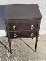 Closed antique spool cabinet showing dark wood, two drawers with brass ring handles, and tapered legs.