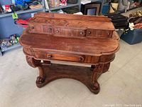 Front and angled view of the antique wooden vanity showing its carved legs, claw feet and drawer arrangement.