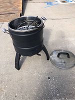 Full view of the Butterball electric turkey fryer with black exterior, steel interior, inner basket and cord, and glass lid placed beside it.