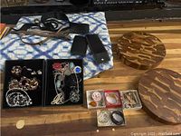 Photo showing the quilt, costume jewelry in boxes, assorted belts, small cases, and two wooden trivets on a wooden surface.
