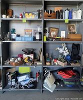 Metal shelving units holding multiple household and collectible items including trays, glasses, framed photos, orchid plant, water bottles, backpack, fire extinguisher, and more.