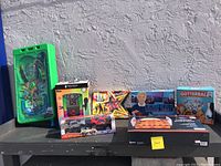 Full lot displayed outside on pavement including green TMNT pinball toy and boxed new games.