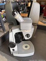 Microscope front-side view showing base, eyepiece, stage, and focusing knob.