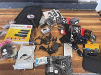 Full view of all items in the lot arranged on floor: Audio Video Selector box, beer tap handle, new charging cables, new sink strainers, black protective case, assorted electronics accessories including mounts, adapters, cables.