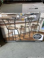 Box showing image of three barstools set against kitchen counter. Barstools have black metal frames with decorative backs and cushioned seats. Label states 'set of 3 barstools'.