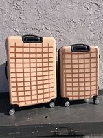 Front view of two rolling suitcases showing beige color with brown grid pattern, different sizes, and four wheels each.