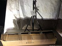 Backdrop stand set up, showing black tripod stand holding a support bar with box in front.