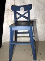Front view of the blue wooden children's chair showing cross-back support and broad seat