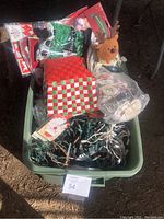 Photo of plastic bin containing various Christmas decorations including string lights, gift bags, small stuffed reindeer, and packaged items