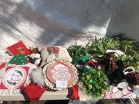 Wide view of various Christmas decorative items on table including pillows, wreath, and holiday figurines.