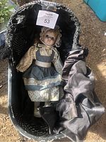 Porcelain doll with blue-gray apron dress inside vintage doll carriage shown from front angle