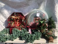 Multiple Christmas wreaths displayed on a table including an octagonal wreath with red berries and pine cones and several smaller wreaths and garlands around it.
