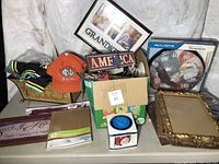 Photo showing Notre Dame hat, Americana signs, multi-photo grandkids frame, AcuRite thermometer, empty frame, plates, and boxed items in a group on floor.