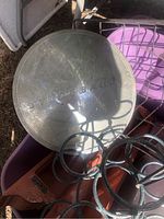 Top-down photo of a round metal automobile hub cap with 'FORD MERCURY' embossed text, shows scratches and wear, sitting inside a purple bin alongside a black metal decorative item.