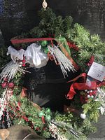 Front view of the large Christmas wreath showing decorative accents including silver icy branches, red ribbons, green and red berries, and white flowers