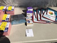 Photo of multiple packs of pink and white index cards, report covers, adhesive items, and label maker tape cartridge on a table.