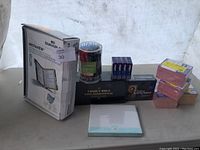 Photo showing a collection of office and religious book supplies including a boxed filing system, a boxed Bible, jars and boxes of pens, index cards, and sticky notes.