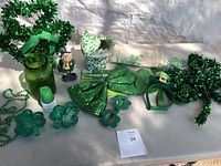 Photo showing assorted St Patrick Day decorations including hats, headbands, shamrock items, beads, a figurine, green glass jar.
