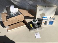 Overview photo showing multiple telephones, boxes, and accessories on a grey surface.