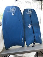 Two Body Glove blue water boards standing upright, one with wrist leash attached, one without.