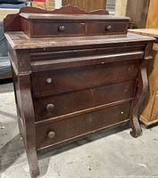 Front view of antique solid wood dresser showing three large drawers and two smaller top drawers with round wooden knobs. Surface has scratches and wear marks.