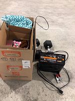 Photo of Schumacher battery charger, 20 lb dumbbells, and a cardboard box containing various items including a hand trimmer.