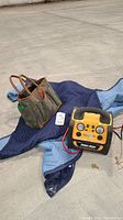 Photo of Power Dome battery charger, gardening tool bag, and blue moving blanket laid out on the ground.