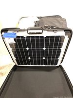 Black folding solar panel with handle and latches open to show photovoltaic cells, suitable for camping use