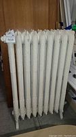 Front and side view of white vintage cast iron radiator heater showing embossed floral decorative pattern on the segments and legs.
