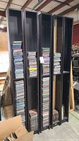 Five tall black CD shelving units with multiple CDs stacked on shelves and some on floor.