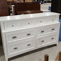 View of the front of the white wooden dresser showing all drawers and silver-tone metal half-moon pulls