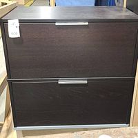 Front view of dark wooden file cabinet with two large drawers and silver handles and base, showing general shape and condition.