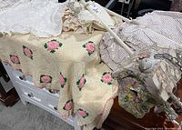 Image showing embroidered pillowcase with ruffled edges, floral linens, crocheted floral blanket, two white metal towel bars, and mosaic birdhouse.
