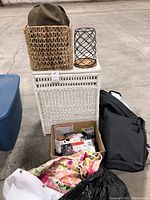 Overview photo featuring the woven basket holding two hats, the white woven laundry hamper, wire candle holder, box of batteries, black waterproof car topper bag, and floral fabric.