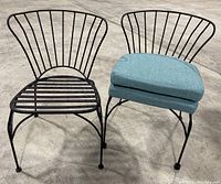 Two black metal chairs side by side, one with blue cushions on the seat and one without cushions.