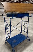Side view of blue painted metal table with scroll work and bottom blue shelf