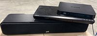 Polk sound bar, Samsung Blu-ray player, and D-Link router stacked together showing their model and brand details.