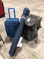 Seahawks folding chair in blue carrying bag with logo, two soft rolling suitcases (navy and black) on concrete floor