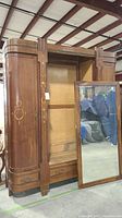 Front view of wooden vintage armoire with mirror panel removed and positioned to the side.