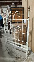 Front and side view of the vintage metal bed frame showing its white painted finish and brass finials.