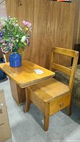 Full view of vintage wooden school desk and chair with a blue vase and faux flowers on top.
