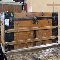 Front view of the vintage wooden storage trunk showing metal bands and central lock with decorative spokes.