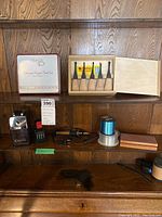 Various tools and accessories on wood shelf including carving tools, presser foot set box, electric pencil sharpener, sewing thread spool, and wooden block.