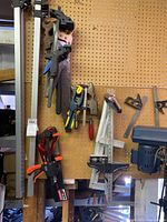 Clamps, saws and measuring tools hung on pegboard including quick grip clamps and hand saws