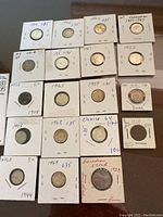 Top view of 19 coins in individual holders with years and some price values handwritten