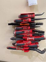 Wall-mounted holder with multiple NWS hand tools with red and black handles, including pliers and crimpers.