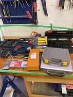 Overview of multiple tool cases including drill bits, screwdriver bits and other accessories arranged on a tabletop in a workshop environment.