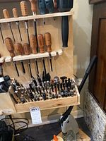 Wooden display rack with leatherworking tools on shelves and manual press on floor